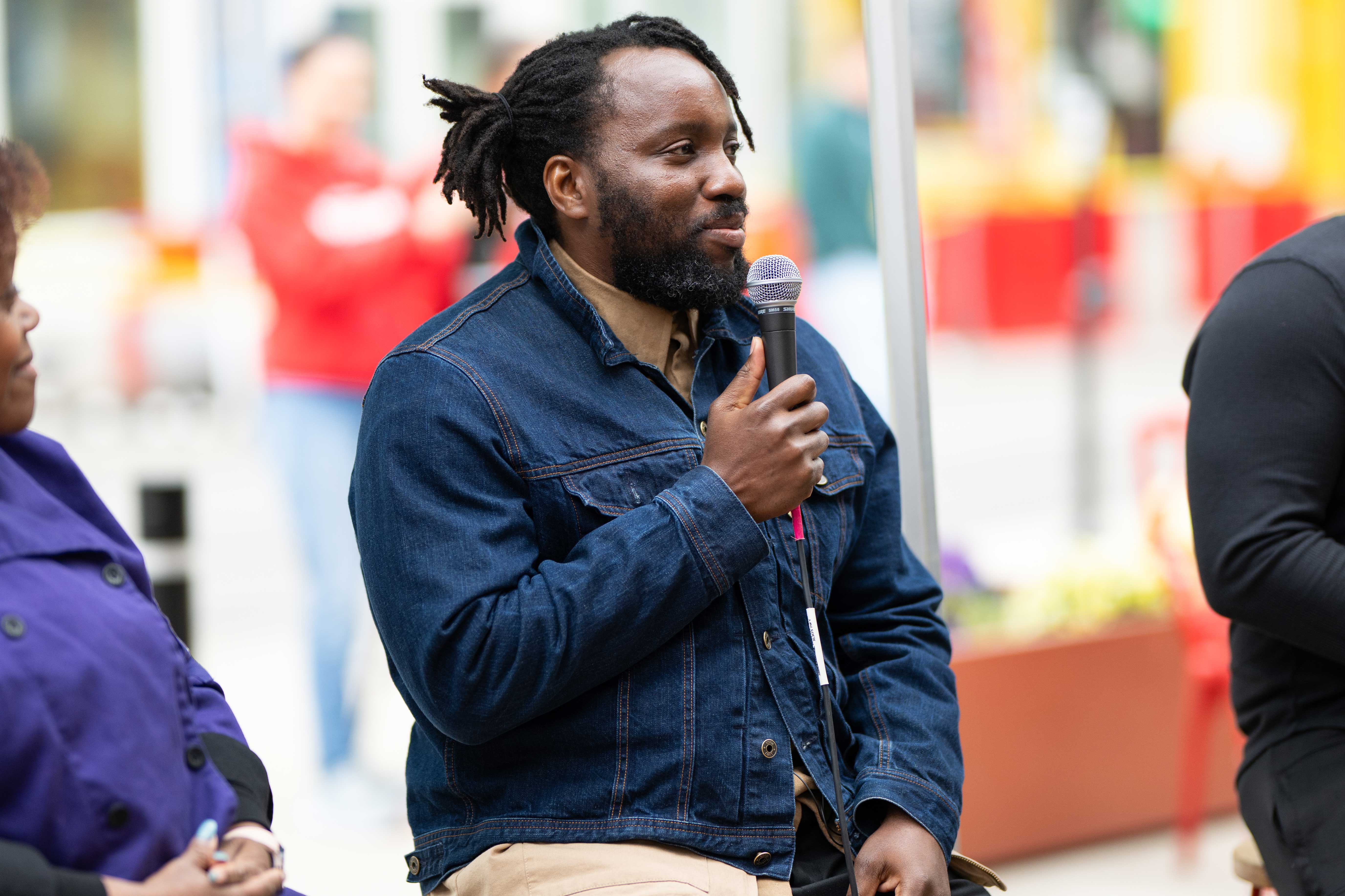 A man sits in a denim jacket with a microphone in hand waiting to speak.